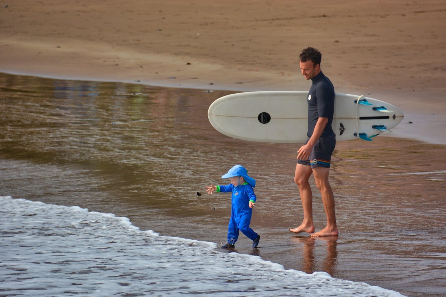 Madre e hijo con tabla de surf en la playa, vacaciones monoparentales en Huelva