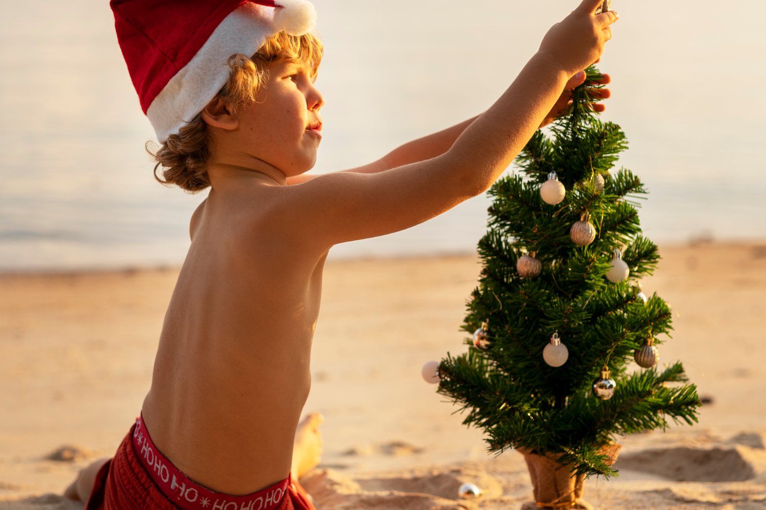 nino decorando arbol de navidad en la playa